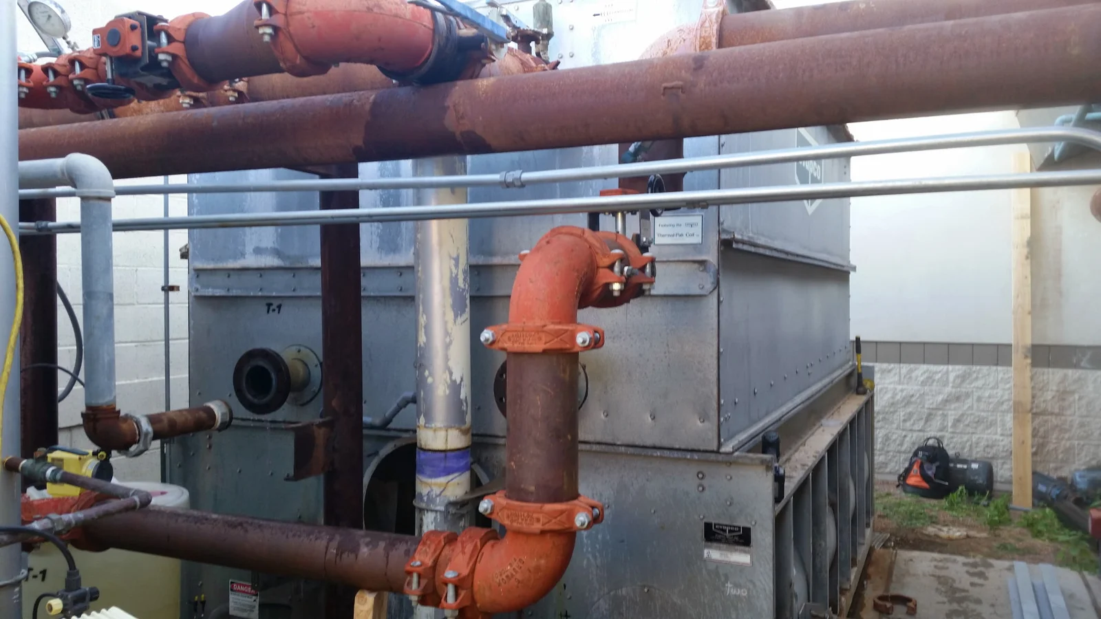 Cooling tower with grooved orange mechanical couplings, rusted steel piping, and gate valves on galvanized steel casing