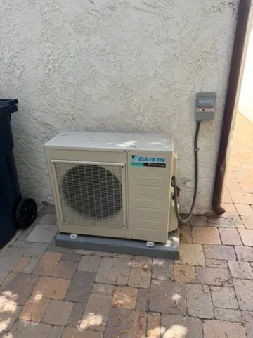 Daikin heat pump outdoor unit installed on concrete pad with electrical disconnect