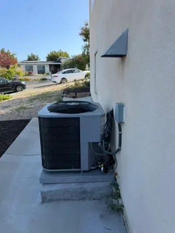 Heat pump unit installed on concrete pad beside white residential building
