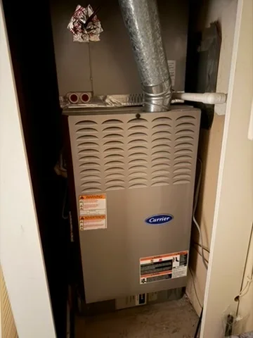 Carrier gas furnace with louvered panel, ductwork, and safety labels in utility closet