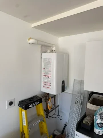 Tankless water heater mounted on wall with venting pipe and electrical connections in mechanical room