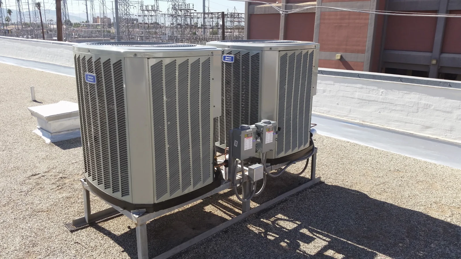 Two American Standard rooftop condenser units on a galvanized steel rack with disconnect boxes and refrigerant lines